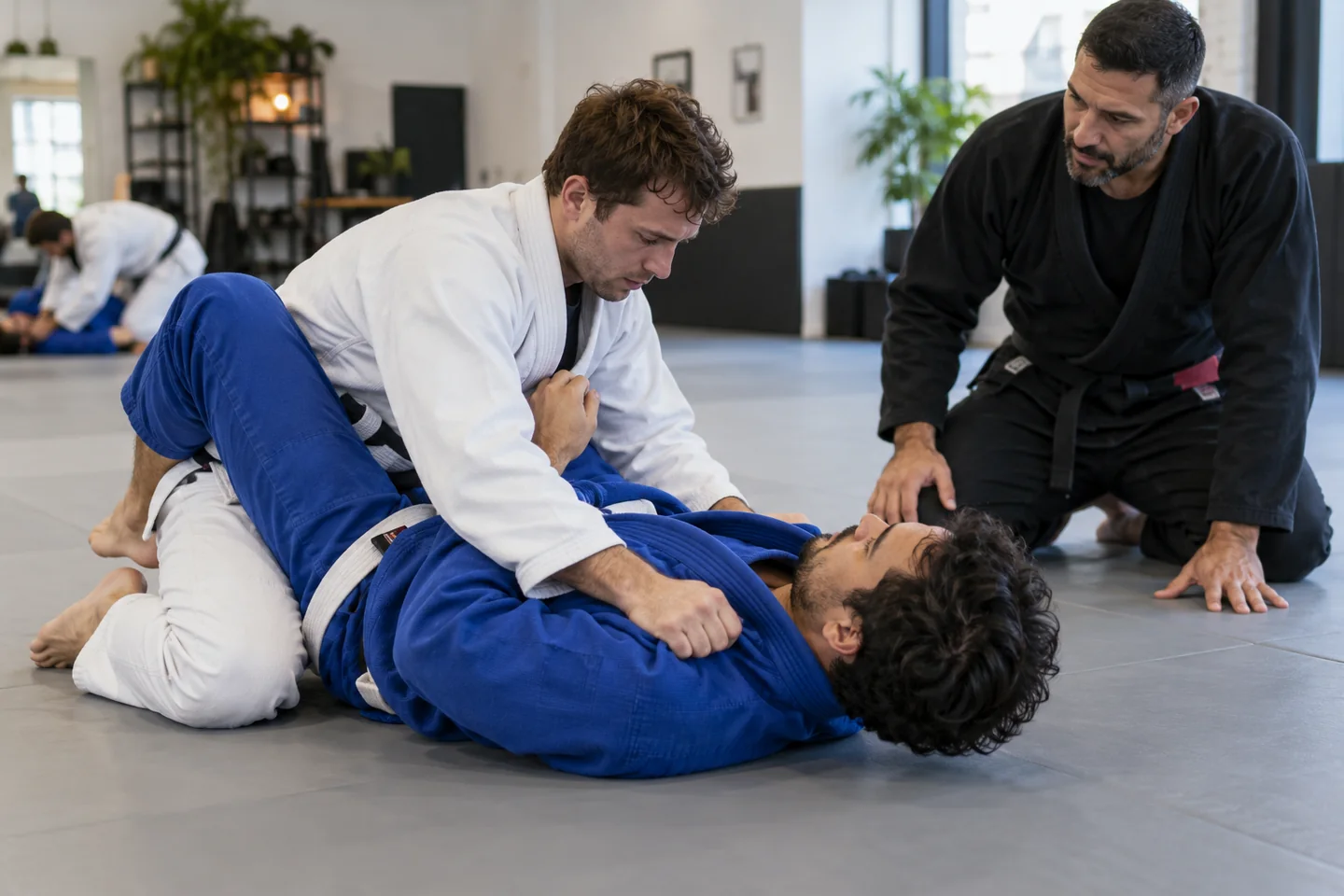 Dwie osoby ćwiczące technikę BJJ powoli pod nadzorem trenera